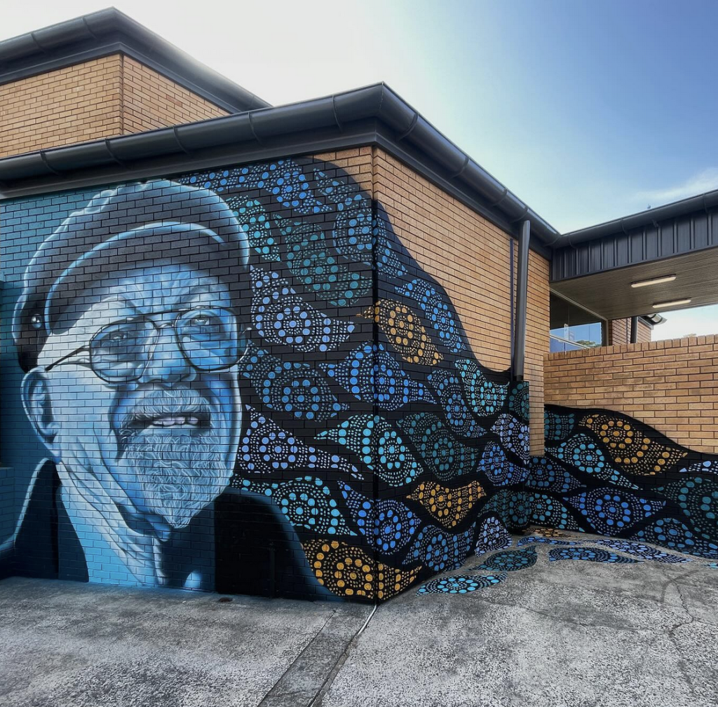 A mural of Vic Chapman, pained in blues on a cream brick wall. 